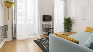 A modern living room with a sofa, a hanging plant, and a television.