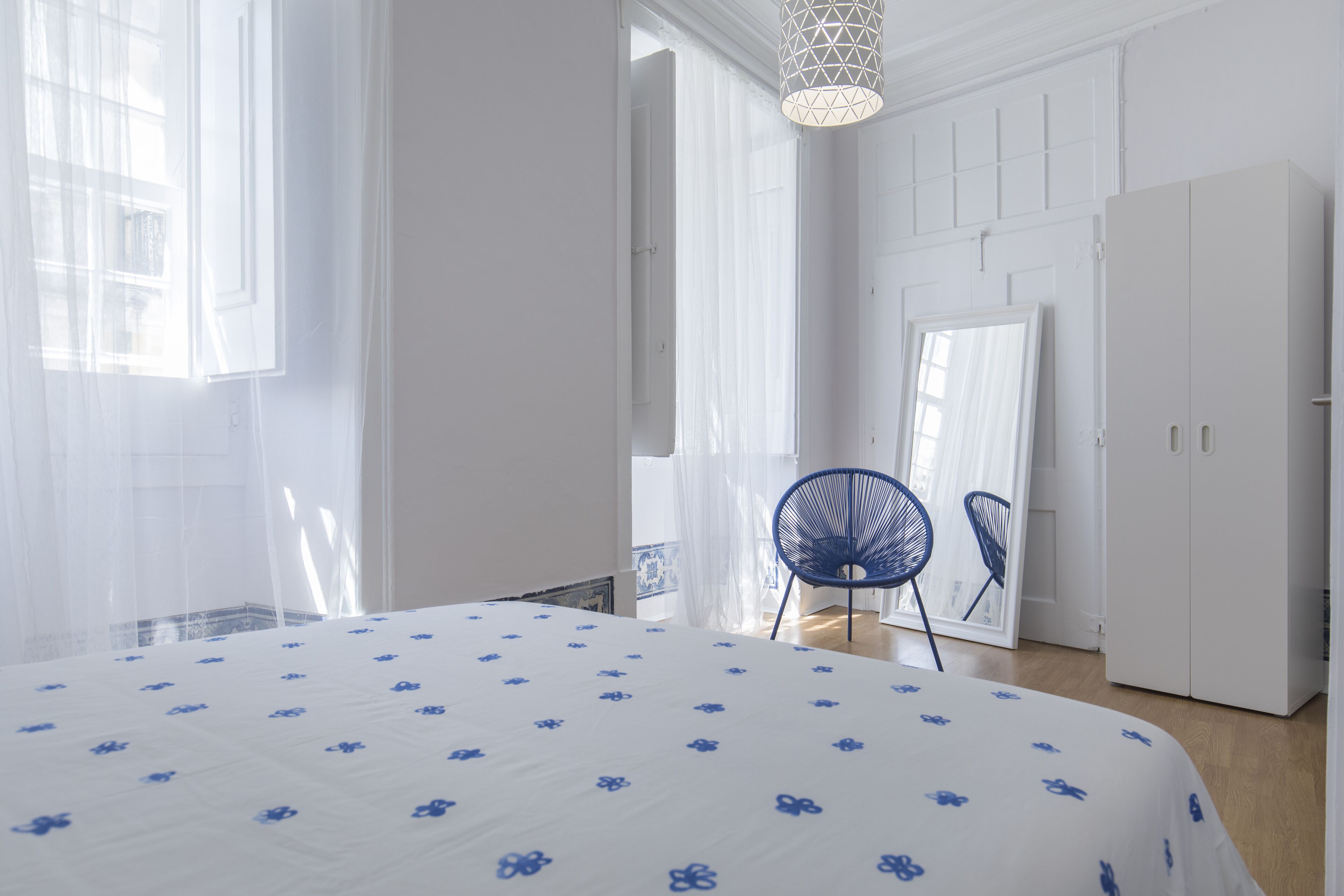 A bedroom with a bed, a chair, a wardrobe, and a hanging light fixture.