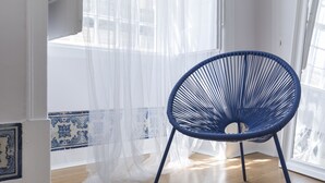 A room with a blue woven chair, sheer white curtains, and a tiled floor.