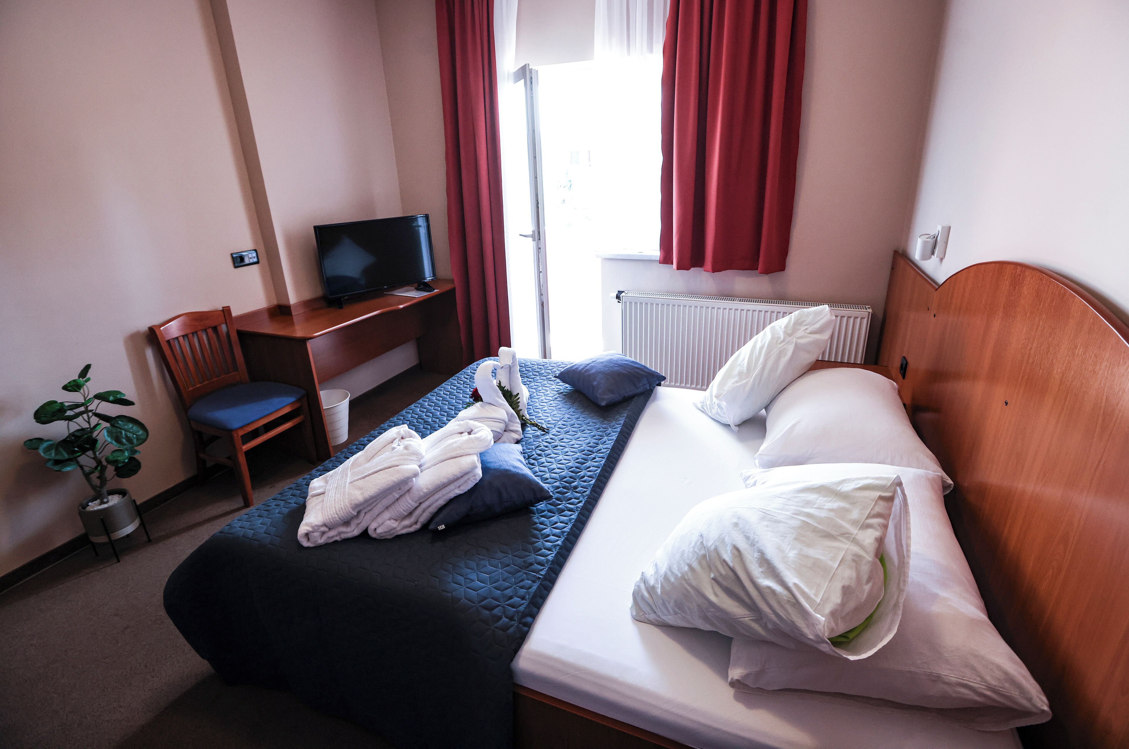 Una habitación de hotel con cama, escritorio con televisor, silla y planta en maceta.