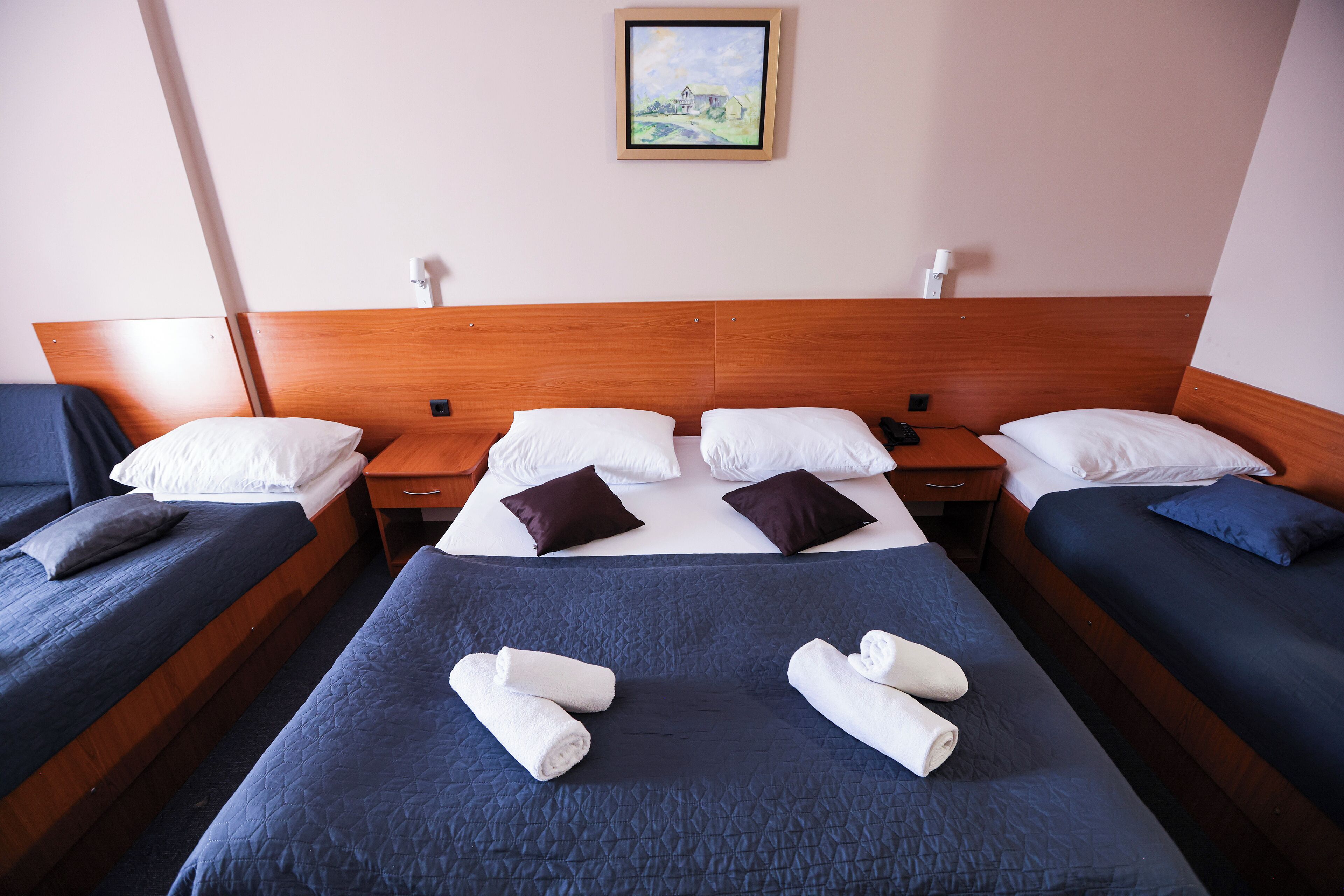 A hotel room with a large bed, two smaller beds, and a painting on the wall.