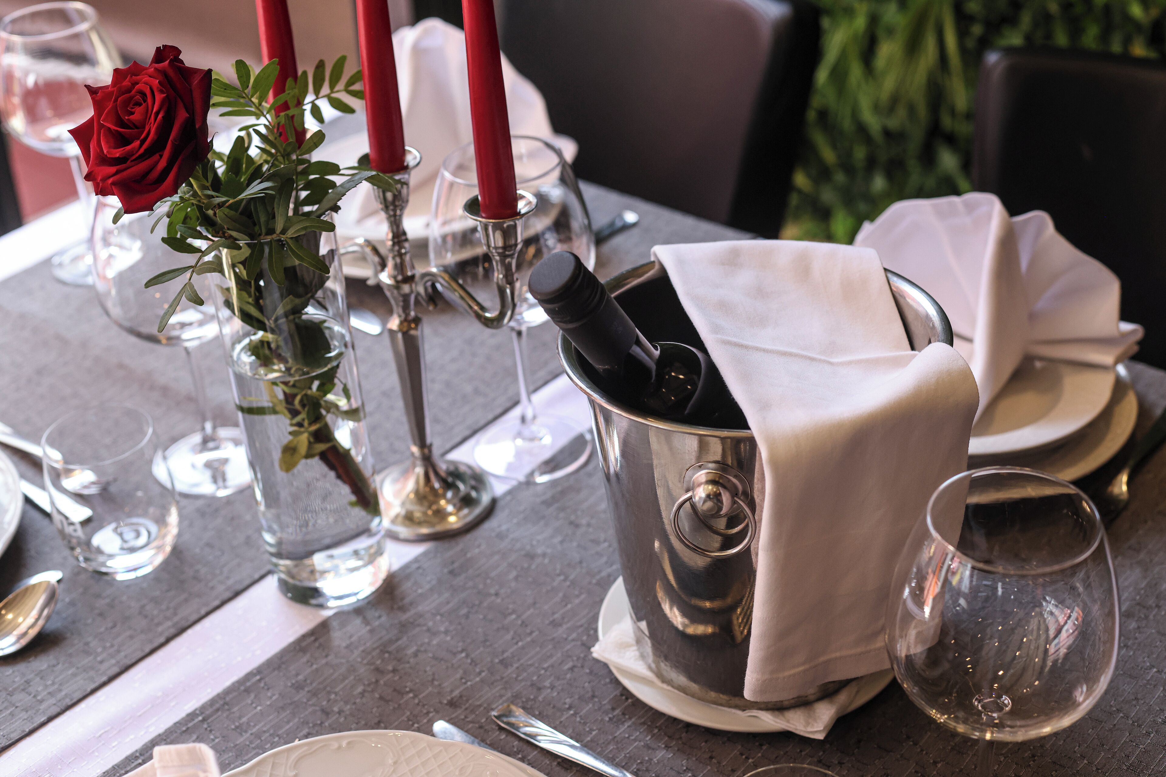 A table set for dining with a vase of red roses, a candle holder, and a metal bucket with a napkin.