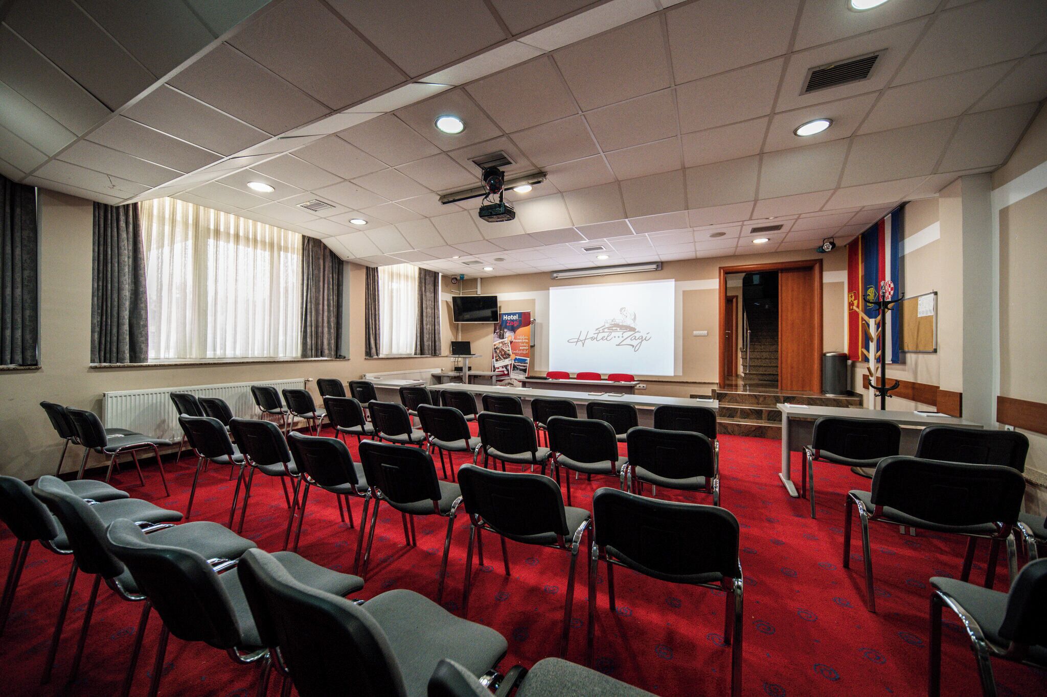 A conference room with rows of chairs, a projector screen, and a presentation area.