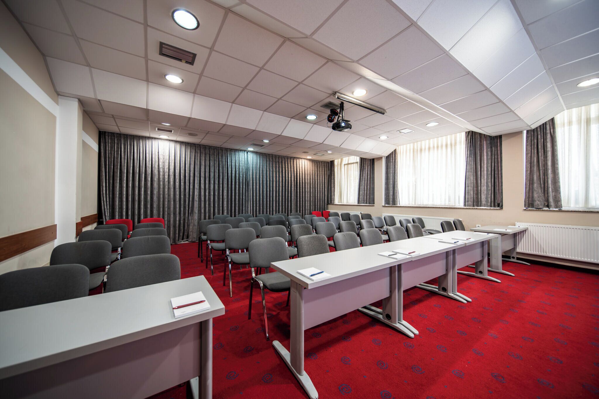 Een vergaderzaal met rijen stoelen, een lange tafel en een beamer.
