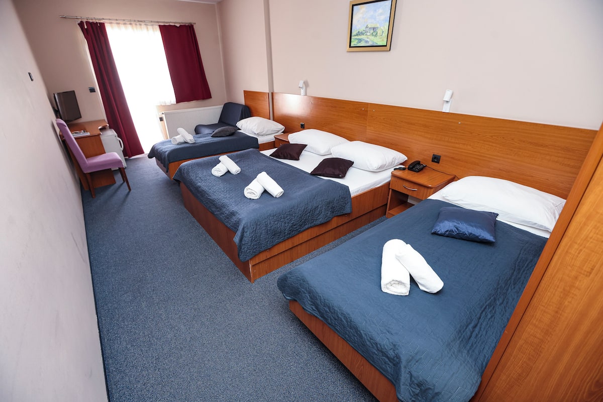 A hotel room with two beds, a desk, a chair, and a TV.