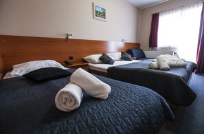 A hotel room with two beds, each with a dark quilted bedspread and pillows, a wooden headboard, a small bedside table with a phone, and a window with curtains. - Hotel Zagi (Oroslavje)