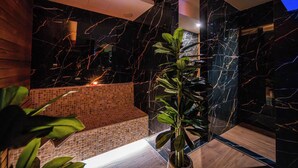 Um banheiro moderno com paredes de mármore preto, um banco revestido em mosaico e um vaso de plantas.