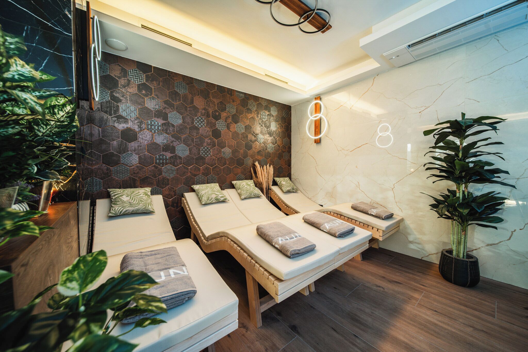 Un cuarto de spa con tres camillas de masaje, un detalle decorativo en la pared y una planta en maceta.