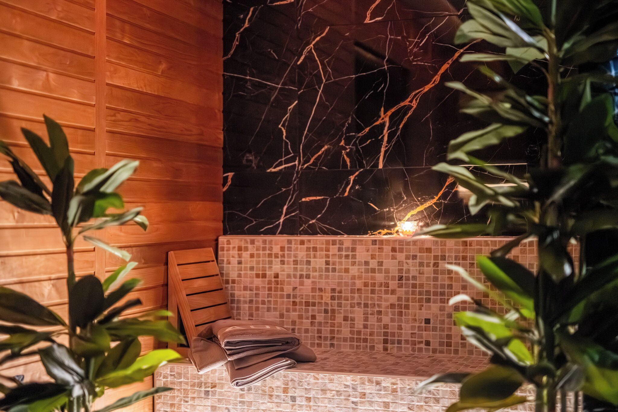 Uma área de spa com parede de madeira, um banco revestido de mosaicos e parede de mármore com uma fissura.