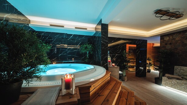 Uma área de spa moderna com hidromassagem, assentos de madeira e plantas em vasos.