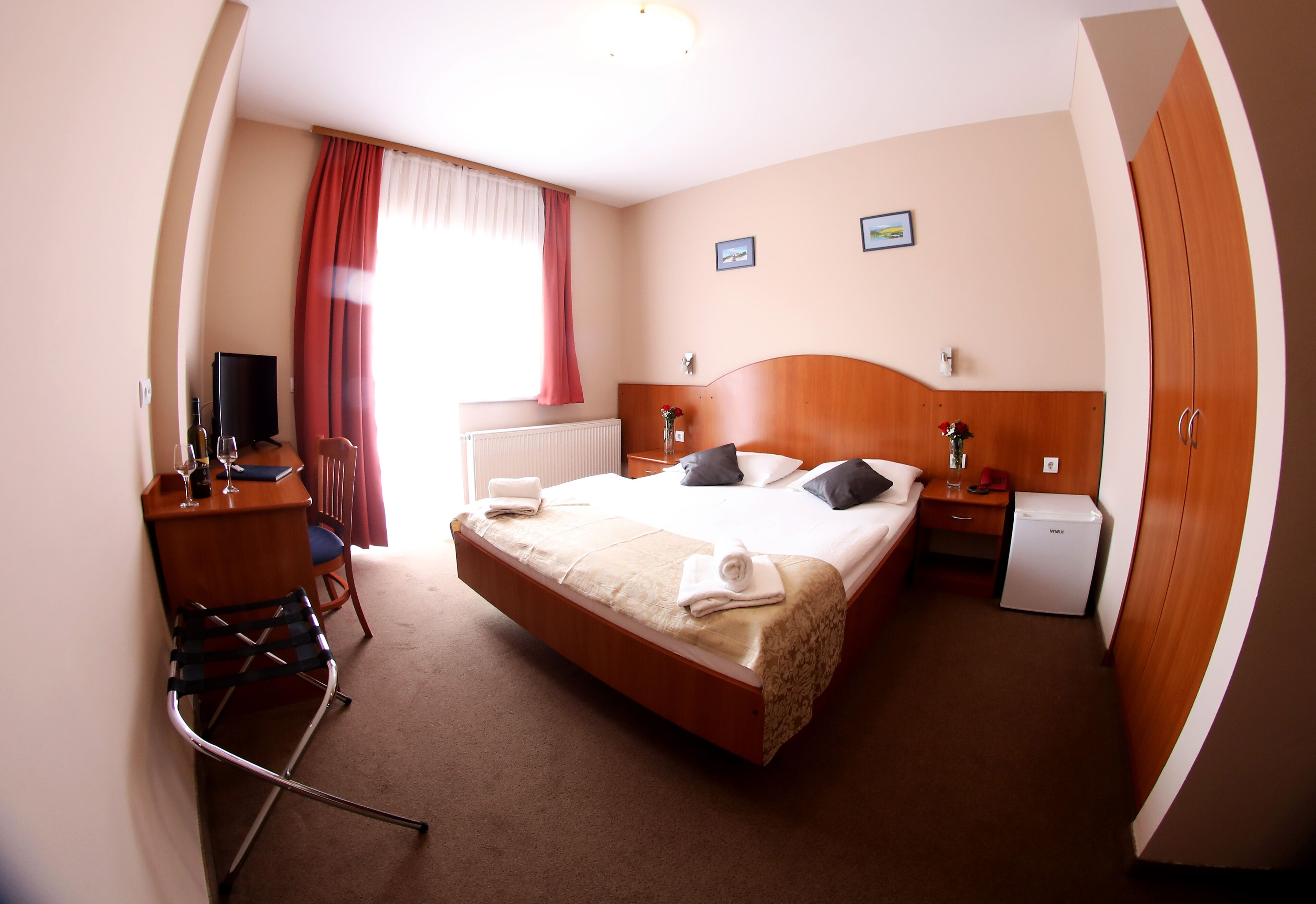 A hotel room with a bed, a desk, a chair, a television, and a small refrigerator.