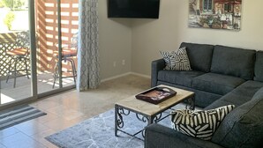A living room with a grey sofa, a coffee table, a flat-screen TV mounted on the wall, and a painting above the sofa. - Charming villa on golf course in Old Town Scottsdale (Scottsdale)