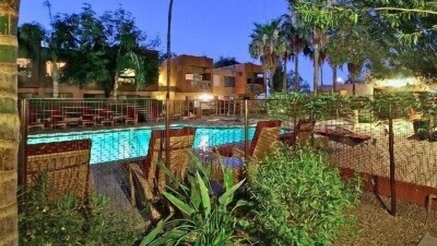 A swimming pool with lounge chairs, surrounded by palm trees and a fence. - Charming villa on golf course in Old Town Scottsdale (Scottsdale)