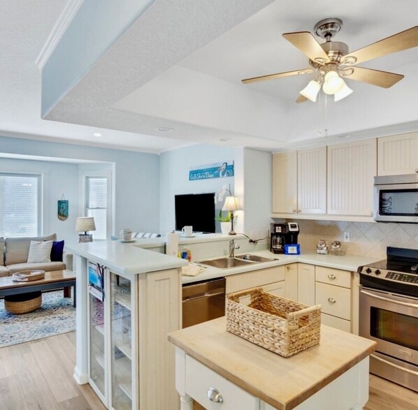 A modern kitchen with a central island, stainless steel appliances, and a ceiling fan.