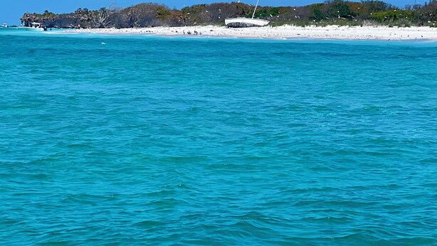 Une plage aux eaux turquoise et limpides, un rivage de sable blanc et un promontoire rocheux visible au loin.