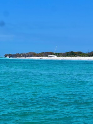 A beach with clear turquoise waters, a white sandy shore, and a distant rocky outcrop.