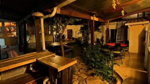 A rustic outdoor dining area with stone flooring, wooden tables, and chairs, surrounded by greenery and a corrugated metal roof. - We are Hostal CasArte Takubamba where you can rest an enjoy! (Sucre, Bolivia)