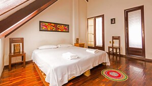 A bedroom with a wooden ceiling, a bed with white linens, a colorful artwork on the wall, and a wooden floor. - We are Hostal CasArte Takubamba where you can rest an enjoy! (Sucre, Bolivia)