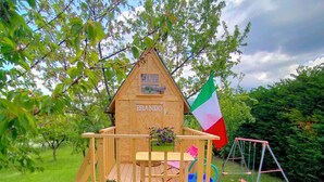 Una casita de juegos de madera con una bandera, un tobogán y columpios.