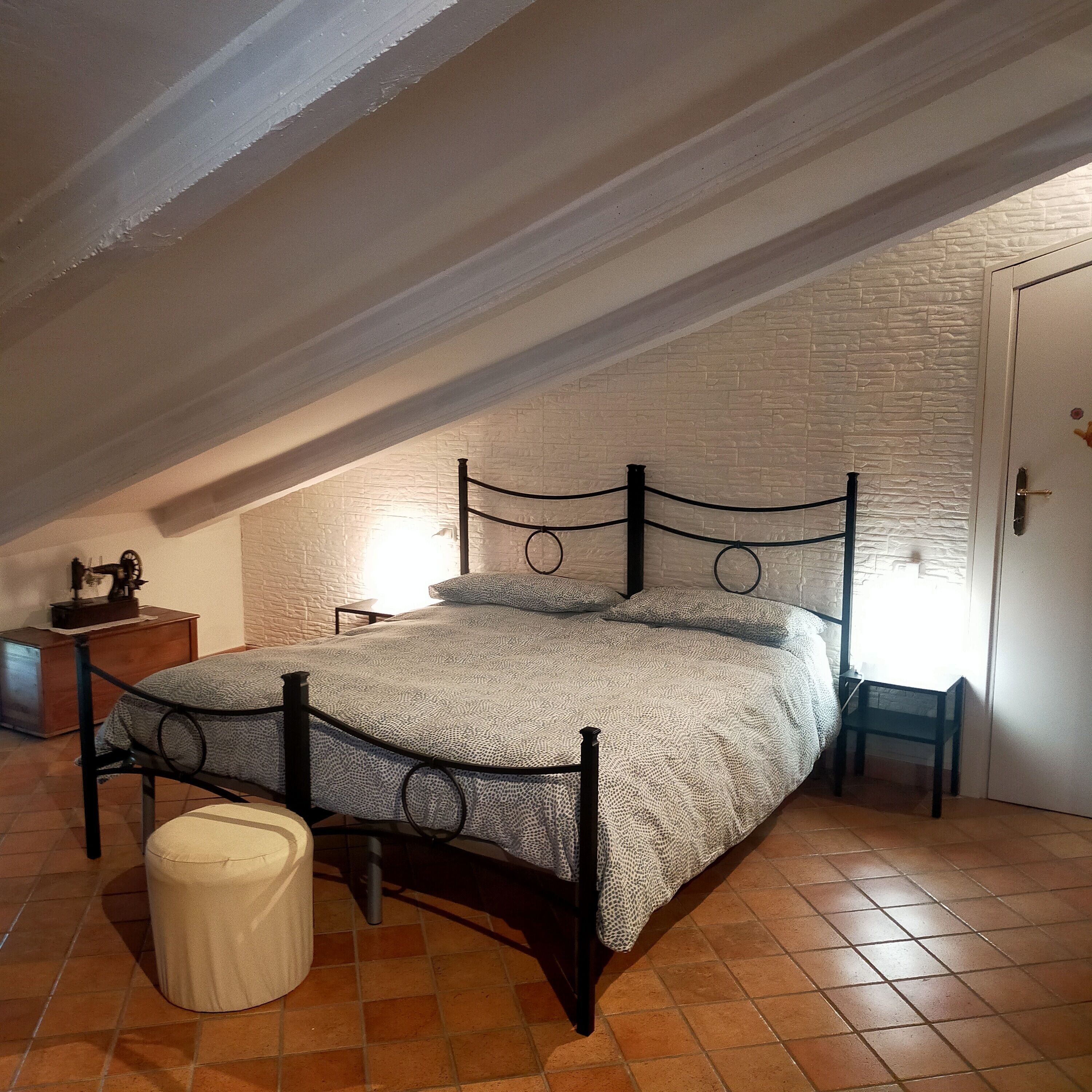 A bedroom with a sloped ceiling, a bed with a patterned bedspread, a nightstand, a small table, and a chair.