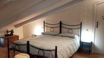A bedroom with a sloped ceiling, a bed with a patterned bedspread, a nightstand, a small table, and a chair.