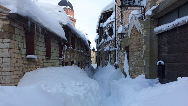 Una calle estrecha con edificios cubiertos de nieve y un callejón visible.