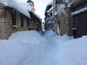 A narrow snow-covered alley between buildings with stone walls and wooden doors. - Mansarda Viti (Frontone)
