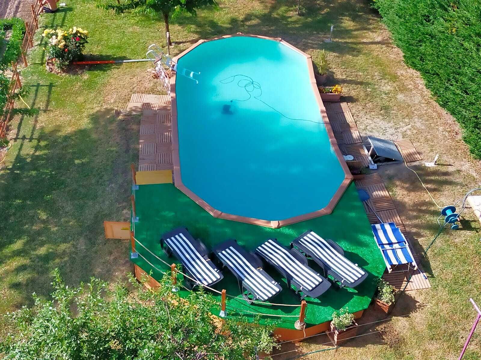 An aerial view of a swimming pool with a deck area, surrounded by grass and trees.
