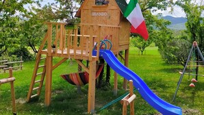 Una casita de juegos de madera con un tobogán, una bandera y una placa con un nombre.