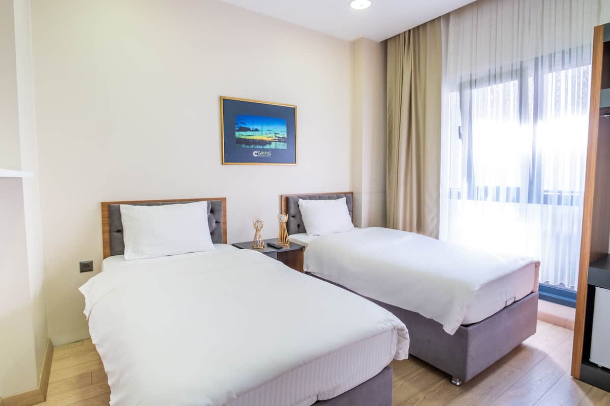 A hotel room with two beds, a nightstand, a framed picture on the wall, and a large window with curtains.