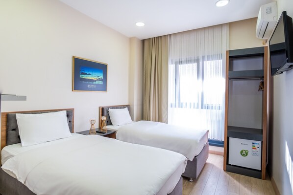 A hotel room with two beds, a nightstand, a TV, and an air conditioning unit.