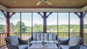 A covered outdoor seating area with a wooden ceiling and large windows offering a view of a forested landscape. - Cozy 2 Bedroom-2 Bath Cottage Near Ski Resorts! Stay at True North Golf Club (Harbor Springs)