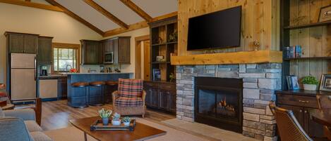 A spacious living area with a fireplace, a television mounted above it, and a kitchen in the background.