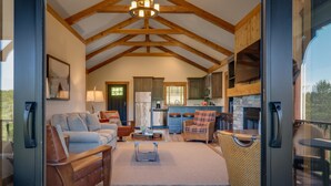 A spacious living area with a high ceiling, wooden beams, a fireplace, and a kitchen with modern appliances. - Cozy 2 Bedroom-2 Bath Cottage Near Ski Resorts! Stay at True North Golf Club (Harbor Springs)