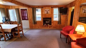 Ein gemütliches Blockhaus-Interieur mit Essbereich, Kamin, Fernseher und einer komfortablen Sitzecke.