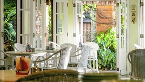 Un coin repas avec des meubles en osier blanc, une petite décoration représentant un voilier et une vue sur une végétation luxuriante à l’extérieur.