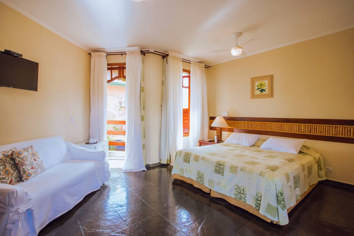 Una habitación de hotel con cama, sofá, televisor y ventilador de techo.