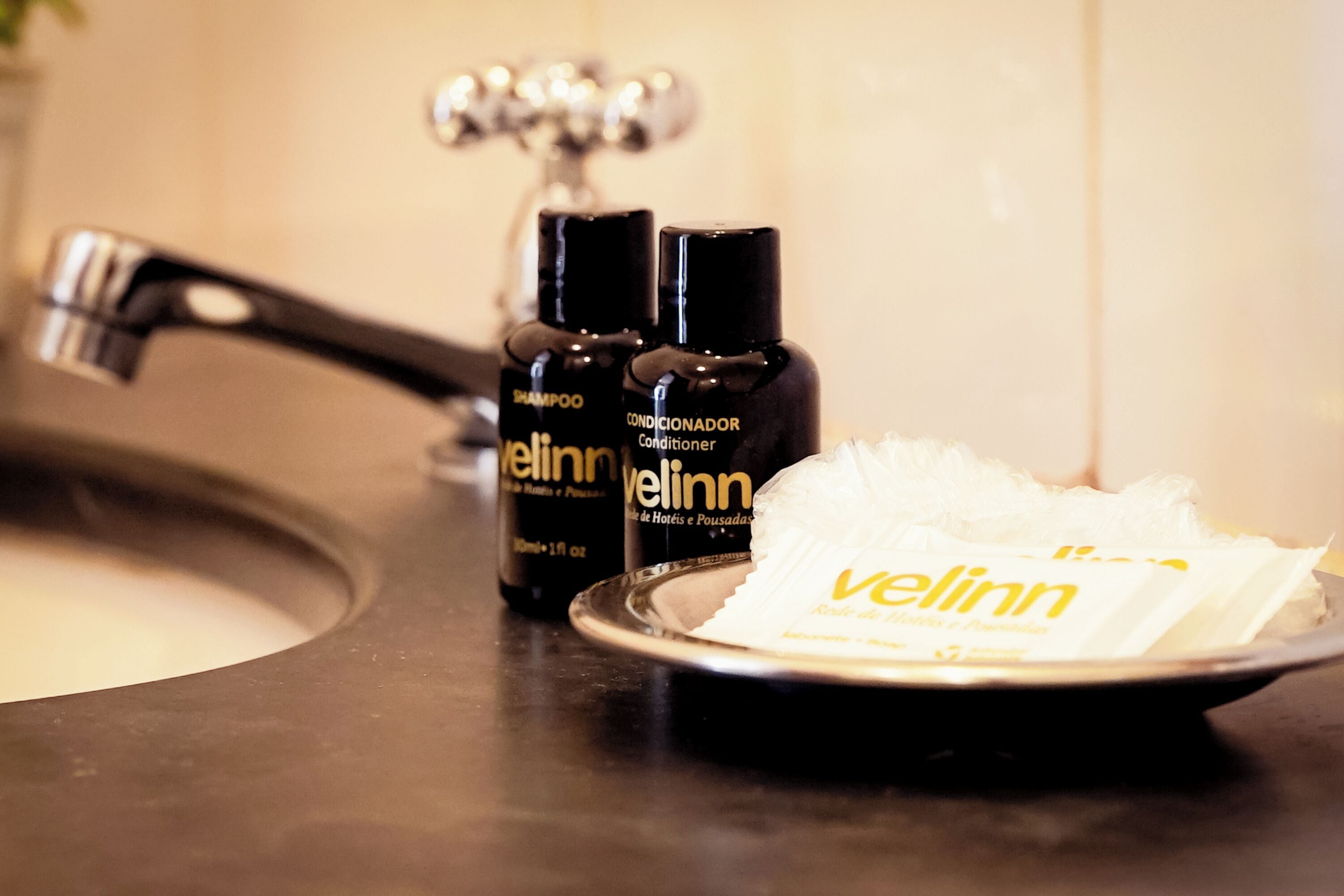 Een badkamermeubel met twee flessen 'Velinn' shampoo en conditioner, een witte handdoek en een zilveren wastafel.