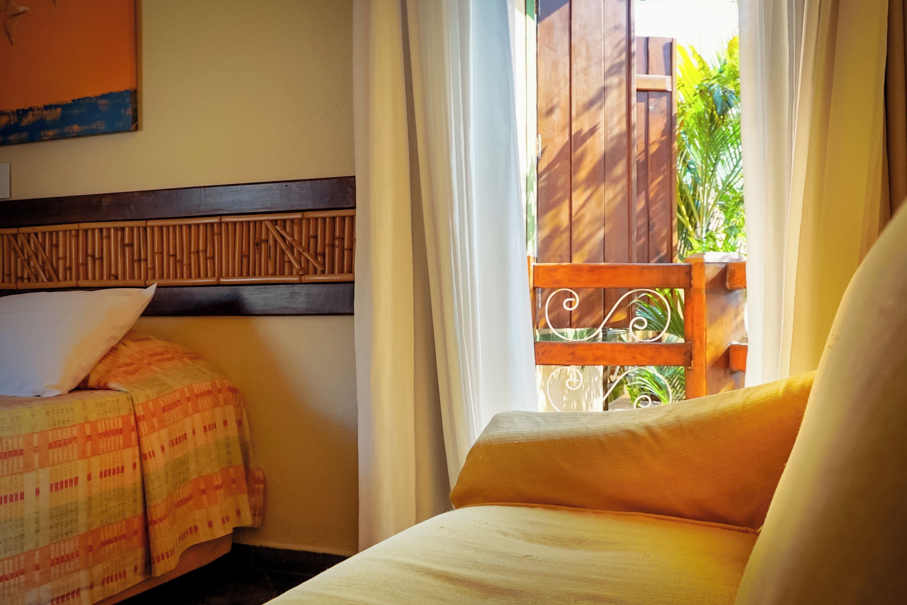 A room with a bed, a chair, and a view of a wooden balcony with plants.