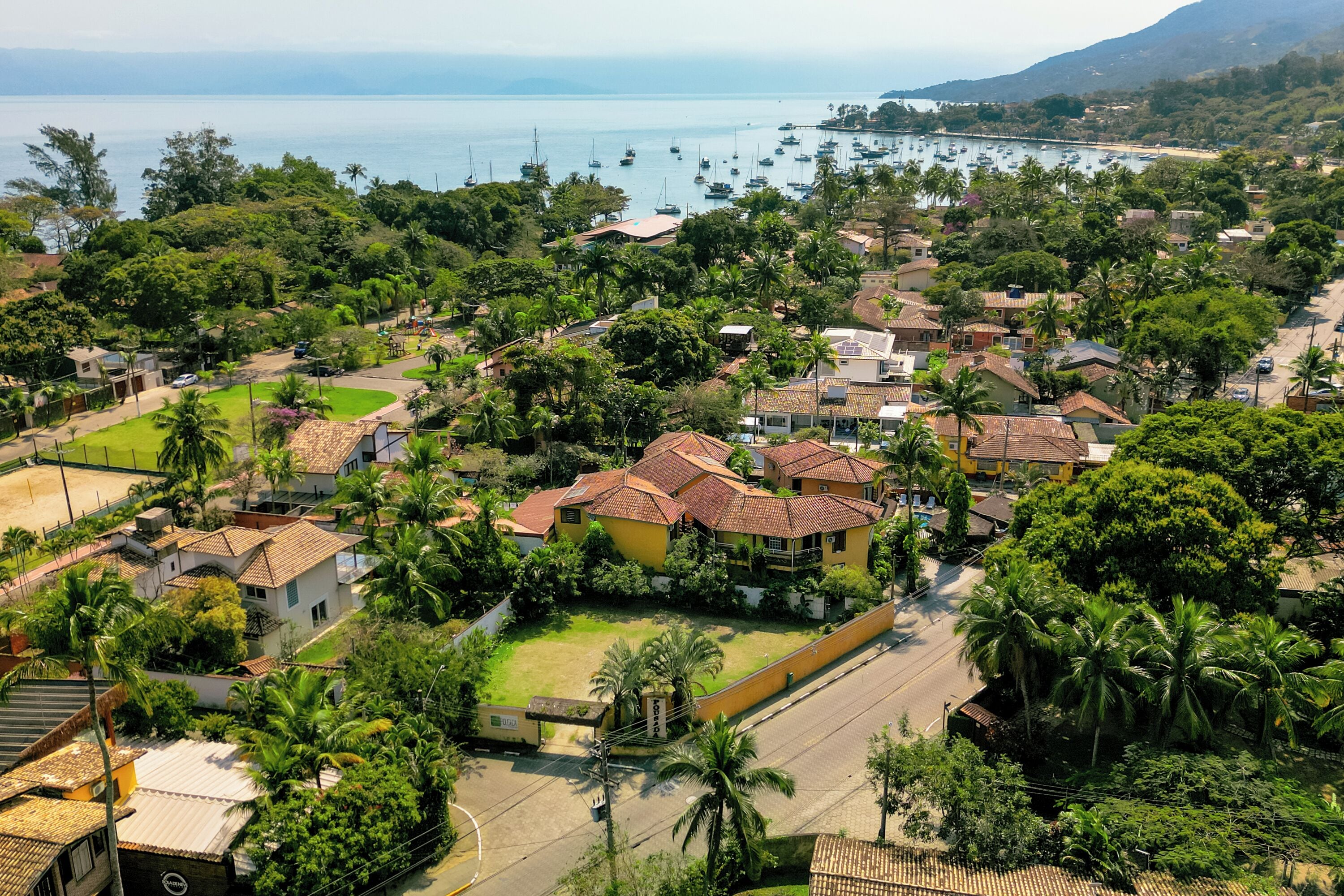 Zona residencial com casas, palmeiras e vista para o mar com barcos.