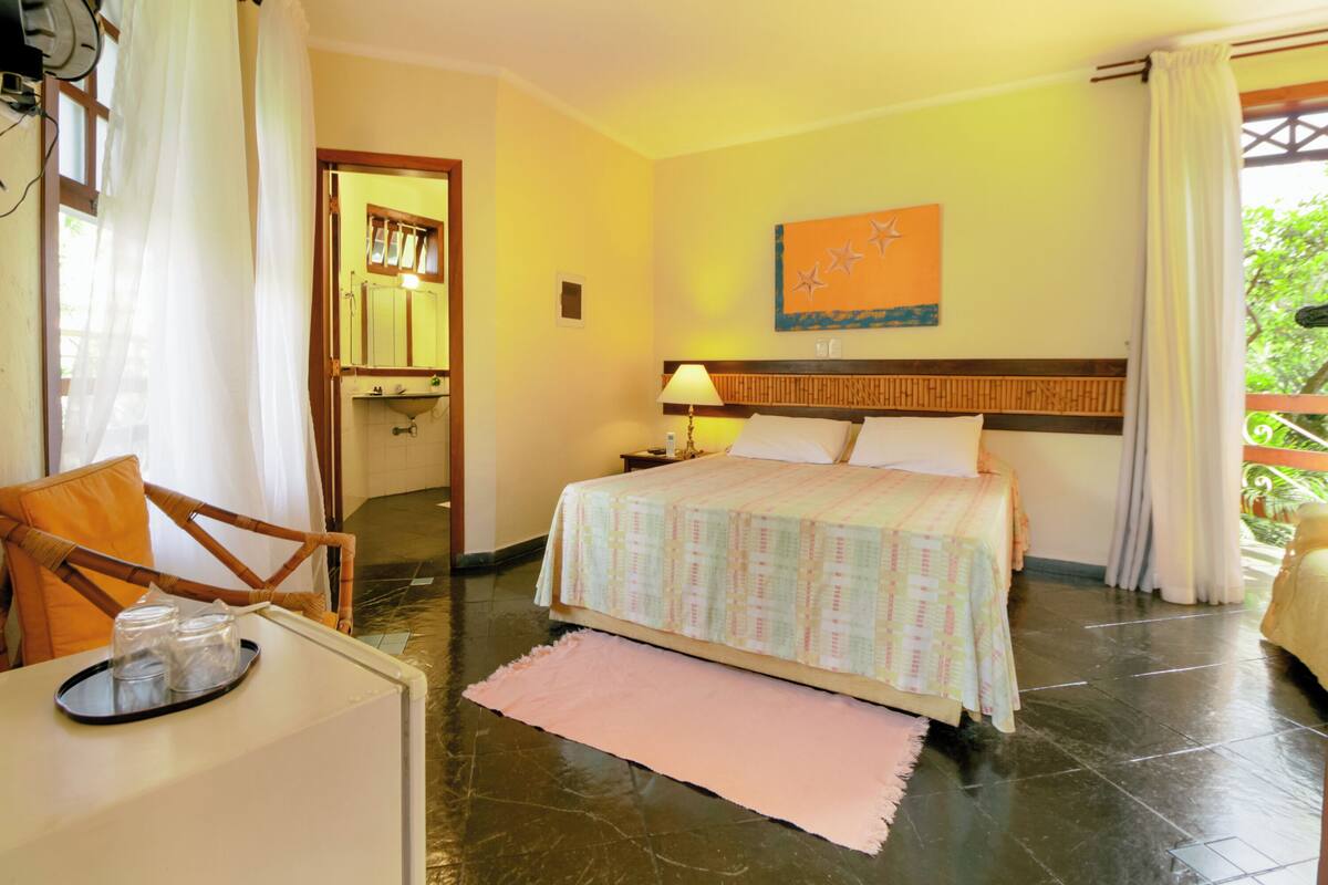 Una habitación de hotel con cama, mesita de noche, silla, mesa con bandeja y ventana con cortinas.