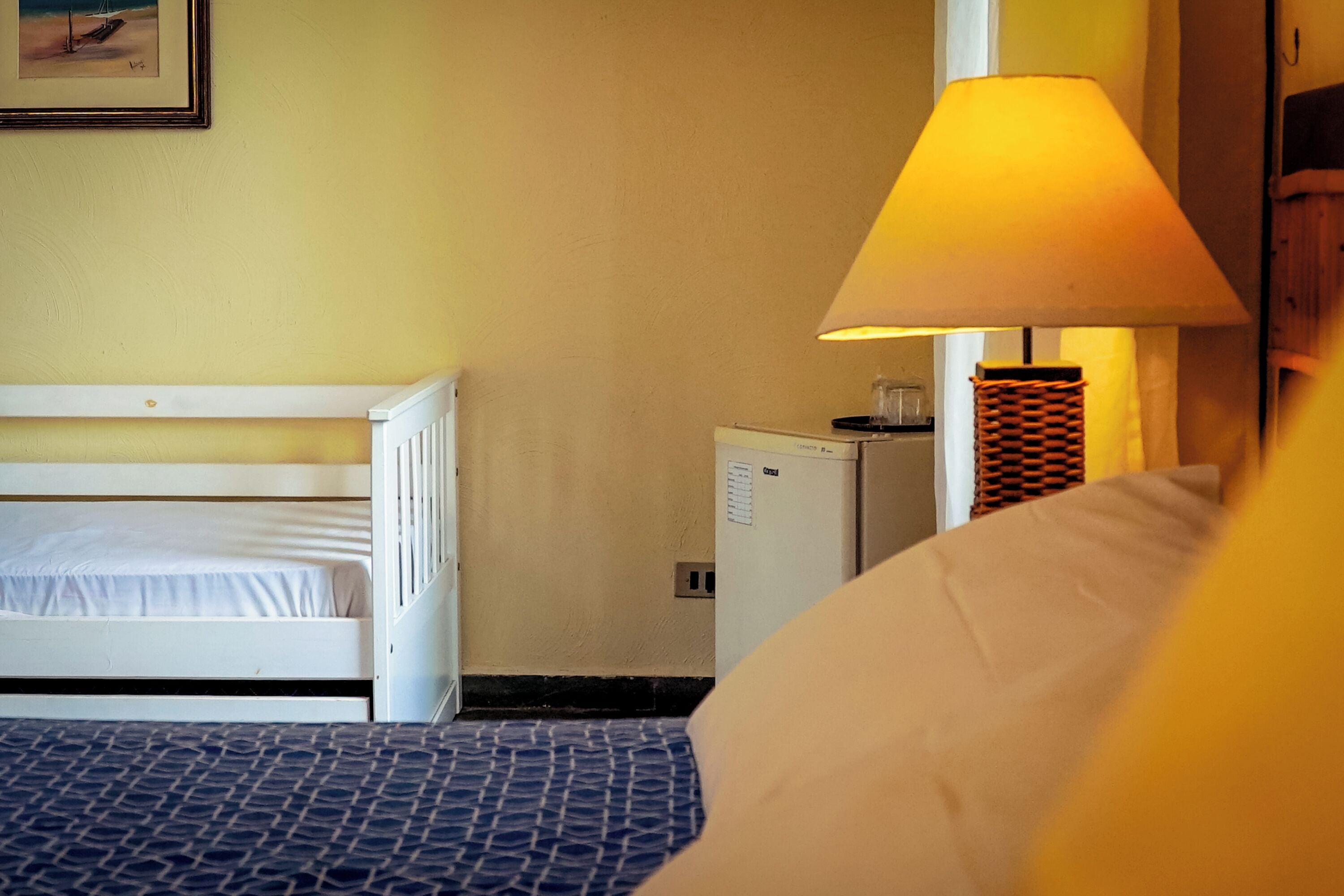 Un dormitorio con una cama litera, una mesita de noche con lámpara, un refrigerador pequeño y un cuadro en la pared.