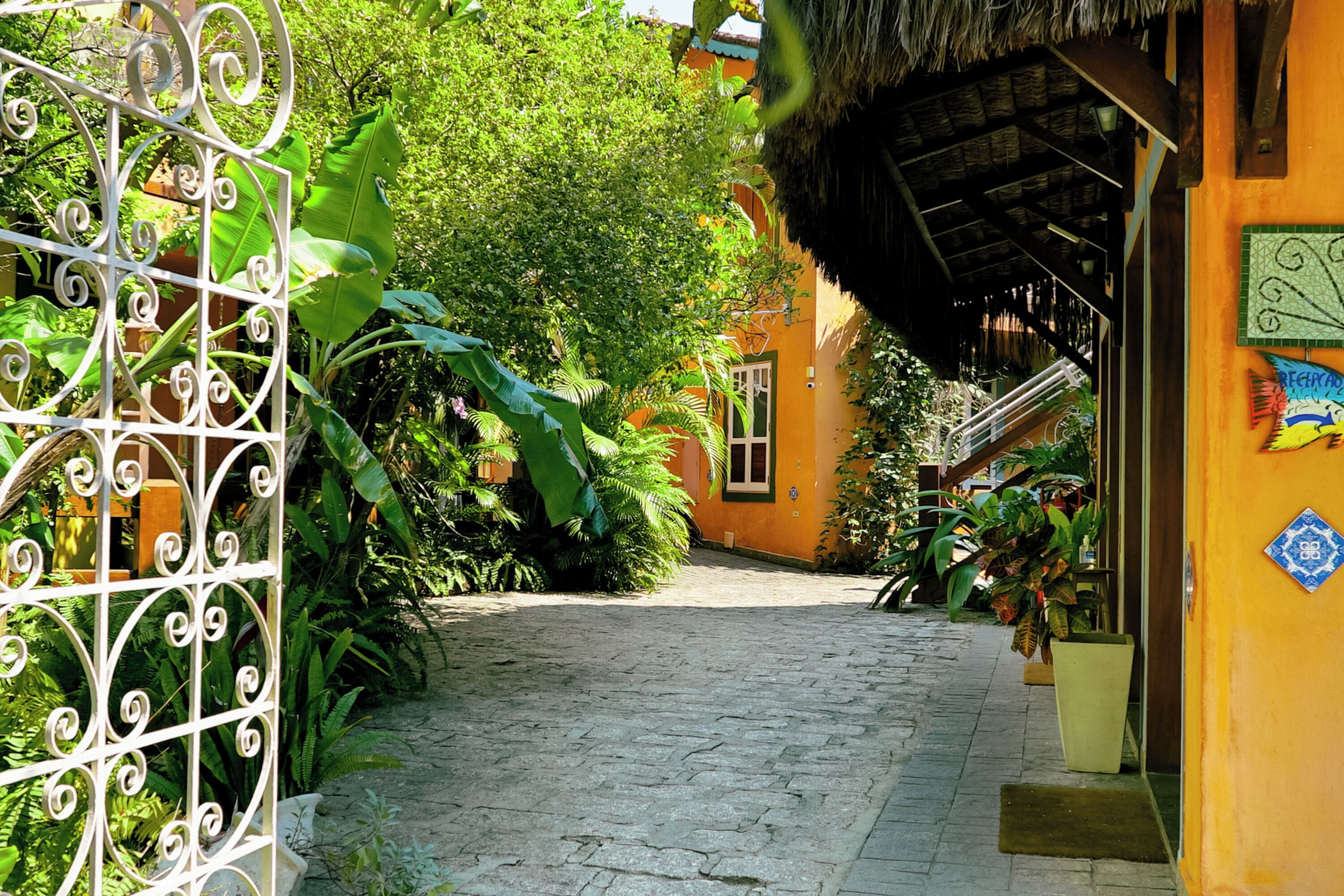 A narrow cobblestone pathway leading to a building with a thatched roof and a decorative metal gate.
