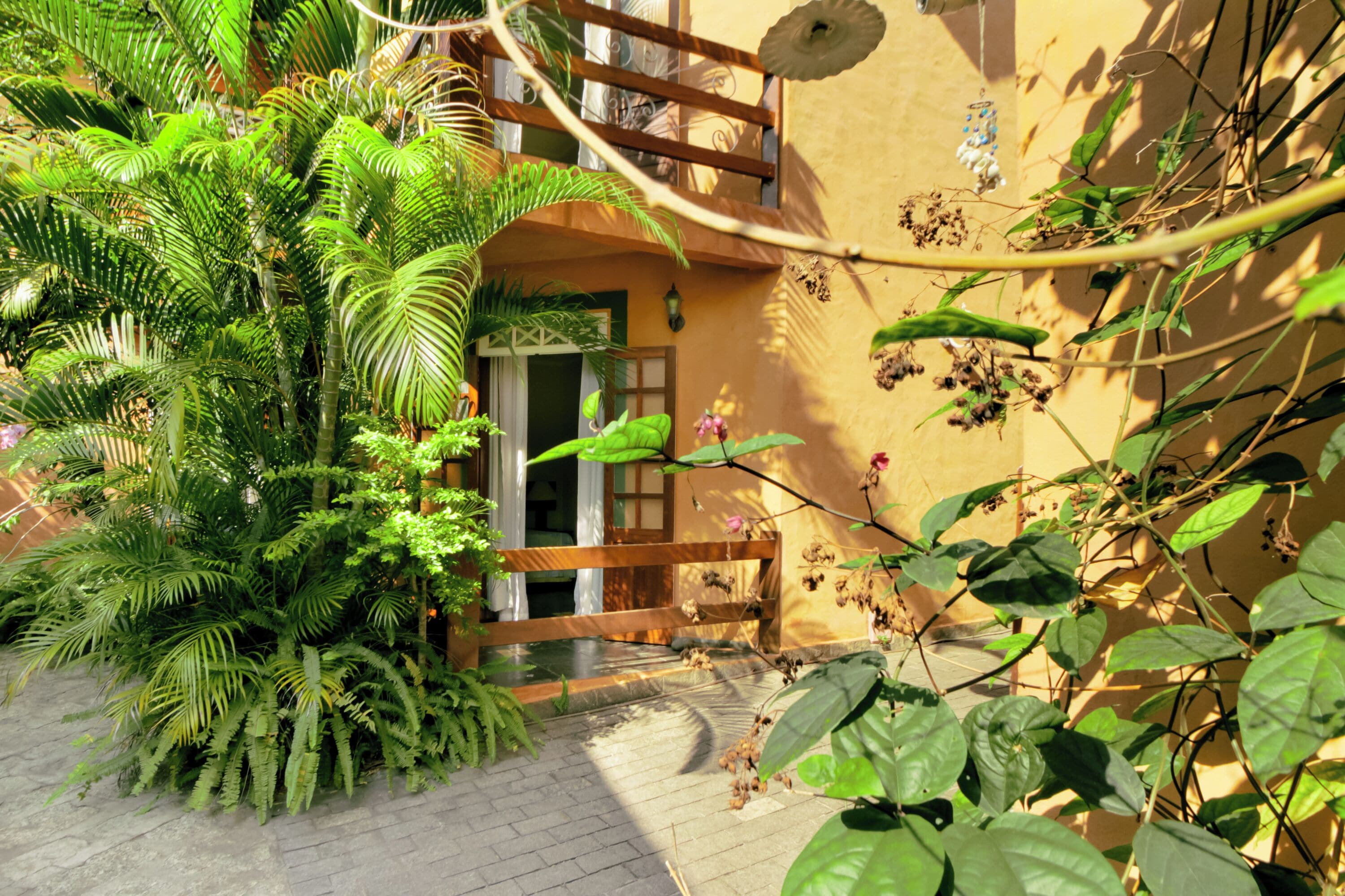 A courtyard with a wooden gate, lush green plants, and a building with a balcony.