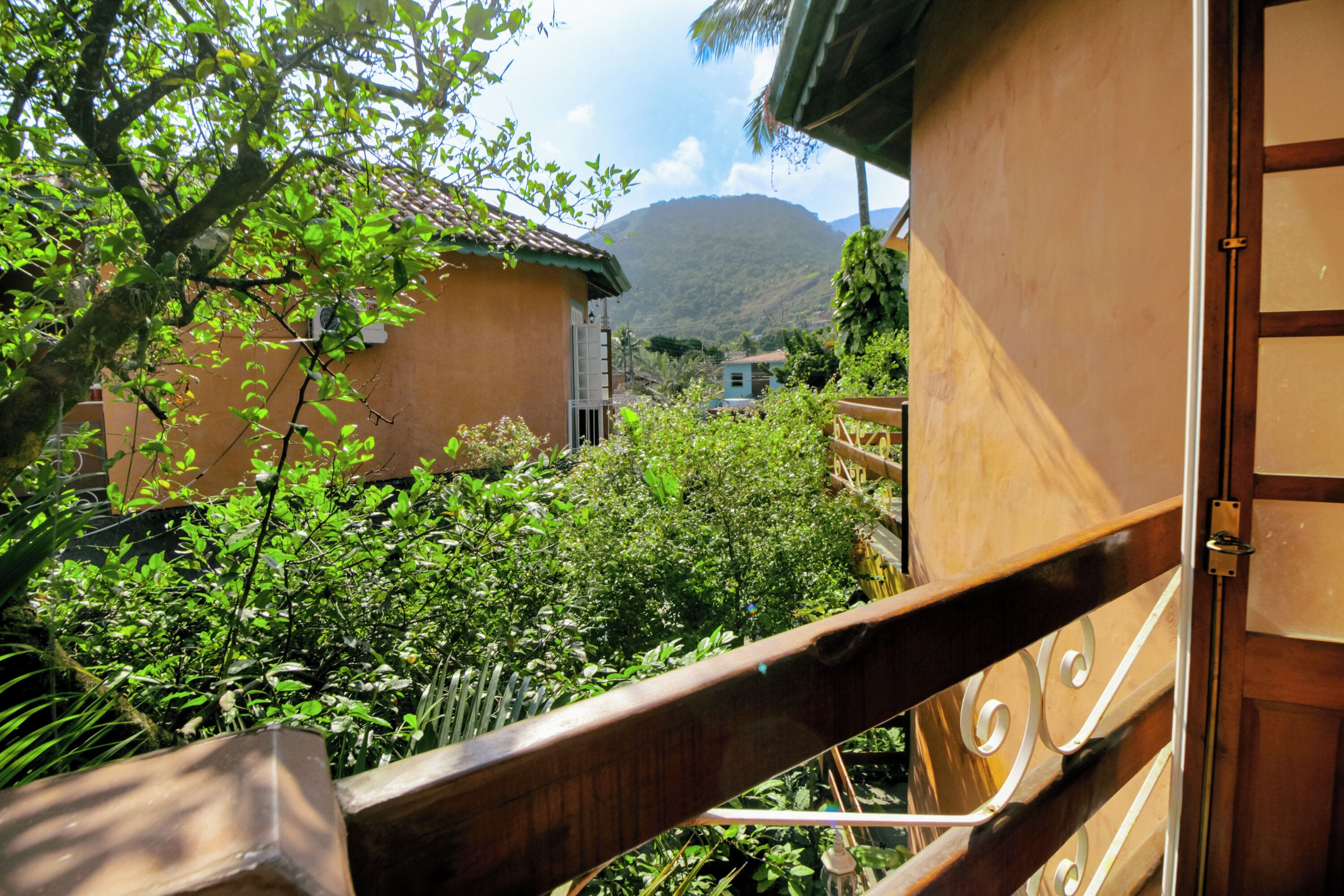 Un balcon doté d’une balustrade en bois, donnant sur un jardin luxuriant et surmonté d’une montagne en arrière-plan.