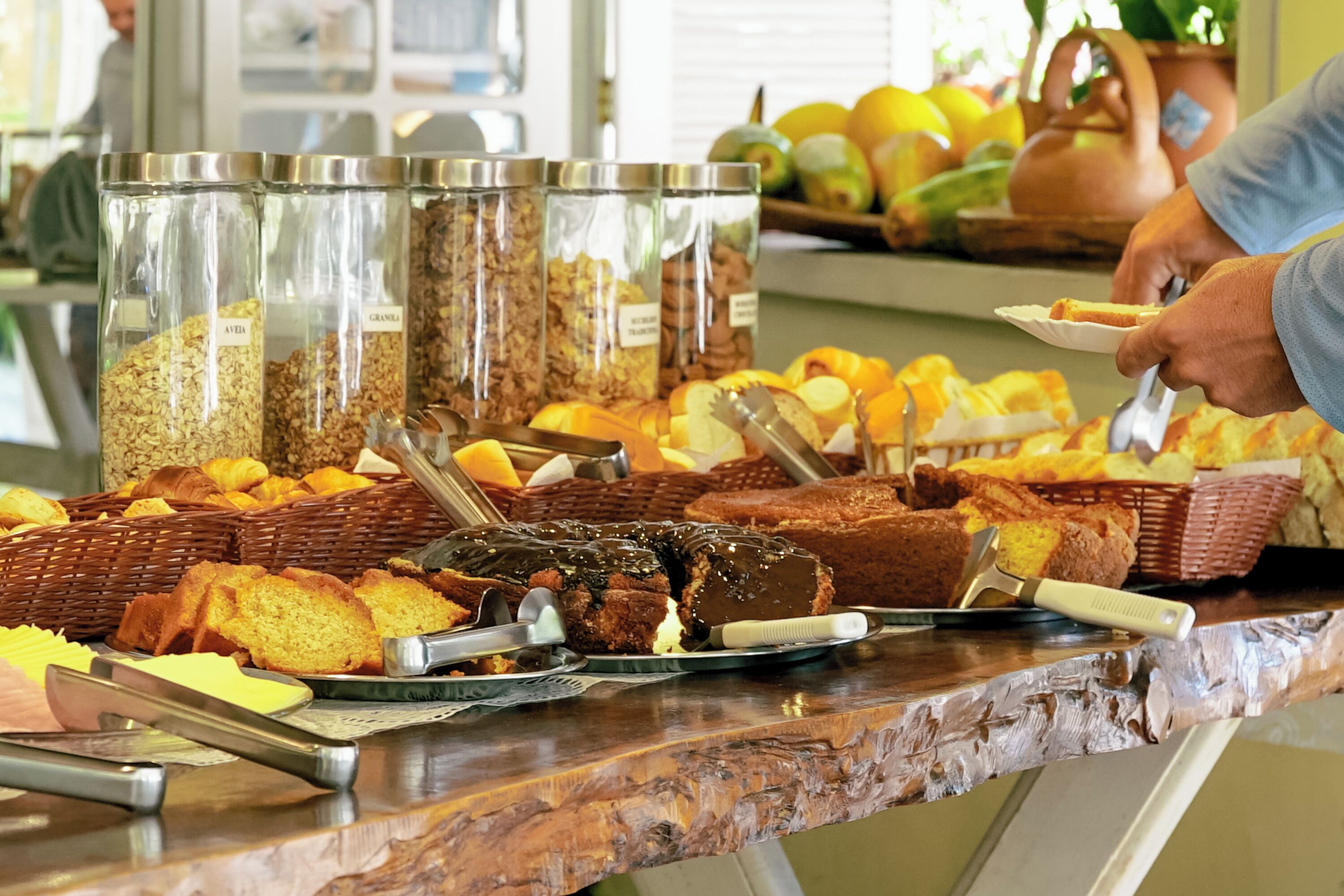 Un buffet proposant une variété d’aliments, notamment du pain et des viennoiseries, ainsi que des récipients contenant du granola.