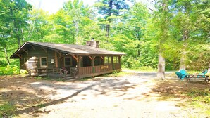 A rustic cabin with a porch, a picnic table, and chairs in a forest setting. - Superior Chalet Hemlock (Wilmington)