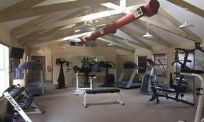 Une salle de sport équipée de divers appareils d’exercice, notamment des tapis de course et des appareils de musculation, située sous un plafond en pente avec des poutres apparentes.