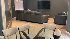 Un salon avec un canapé gris, une table basse en verre et un téléviseur fixé au mur.