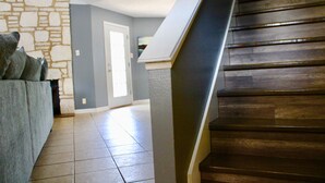 Un escalier avec des marches en bois et une rampe, menant à une pièce dont un mur est en pierre et la porte est grise.